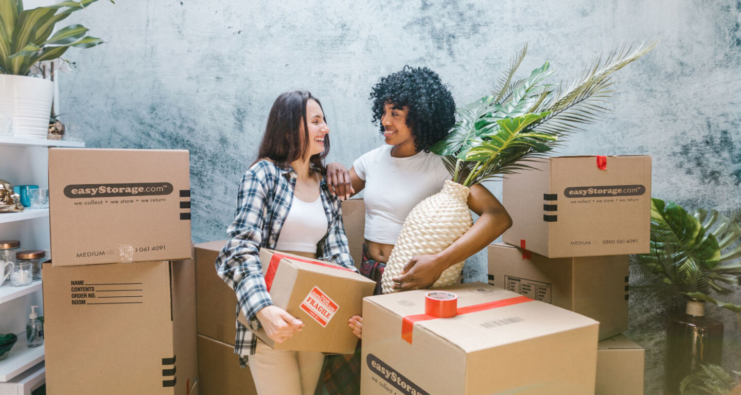 Two women pack belongings into cardboard boxes ready for self-storage 