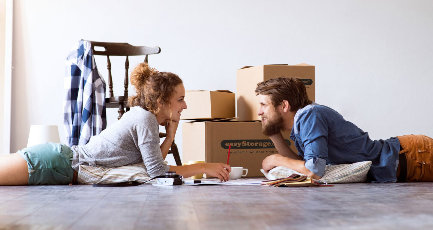 A young couple lay on the floor with cardboard boxes that are ready to go into storage