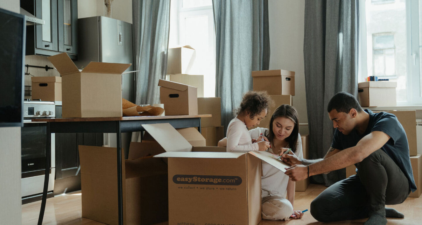 A mother, father and child pack belongings into cardboard boxes ready for self-storage 