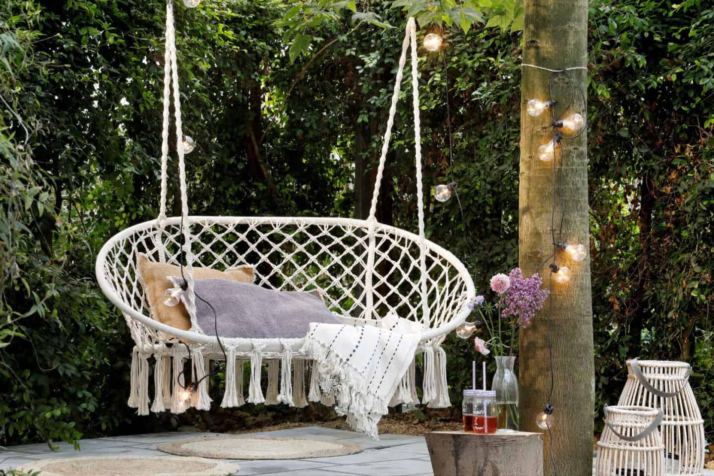 A double macrame hanging chair in a garden beside a tree