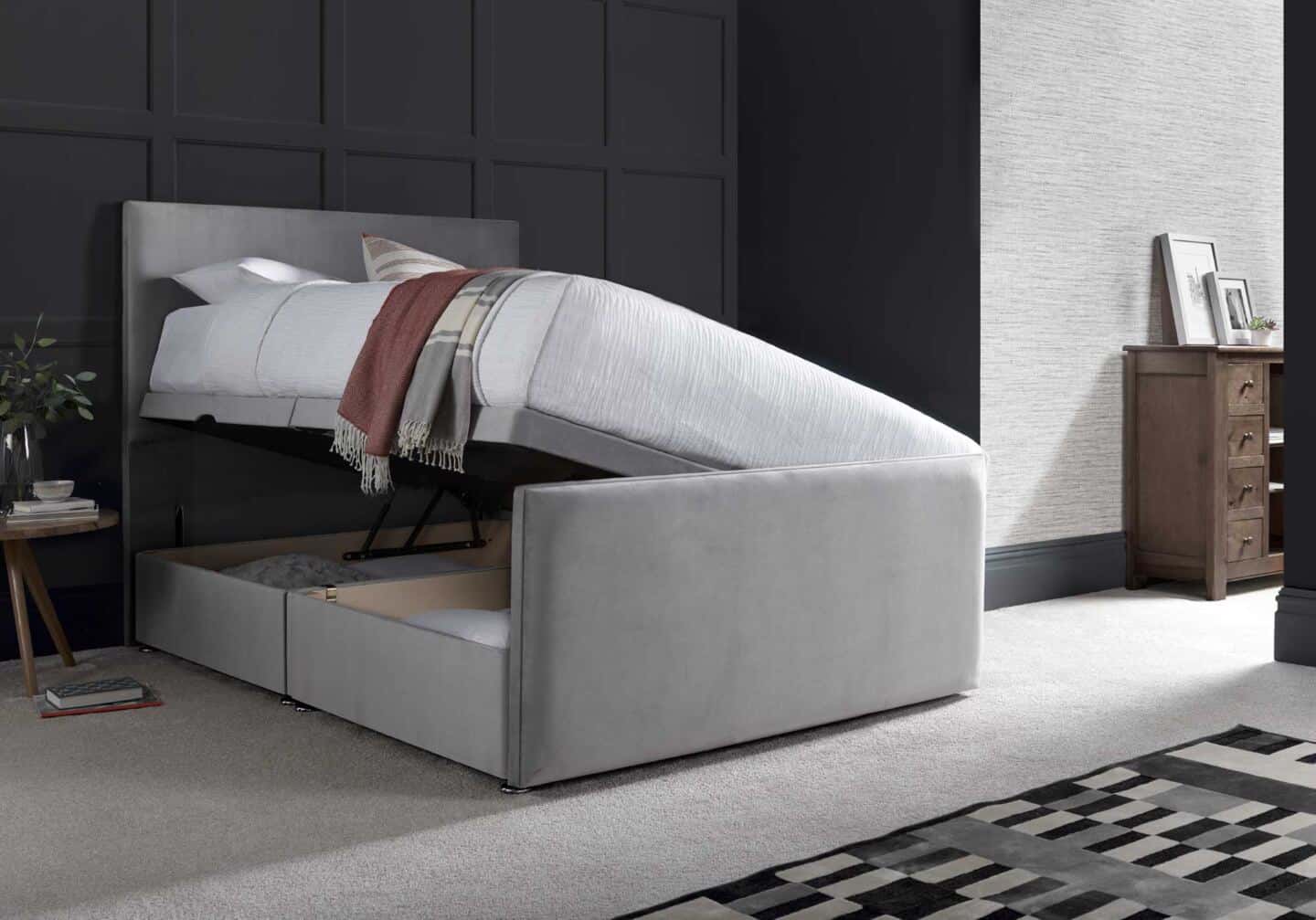 An open ottoman bed full of cushions in a grey bedroom with a panelled wall behind