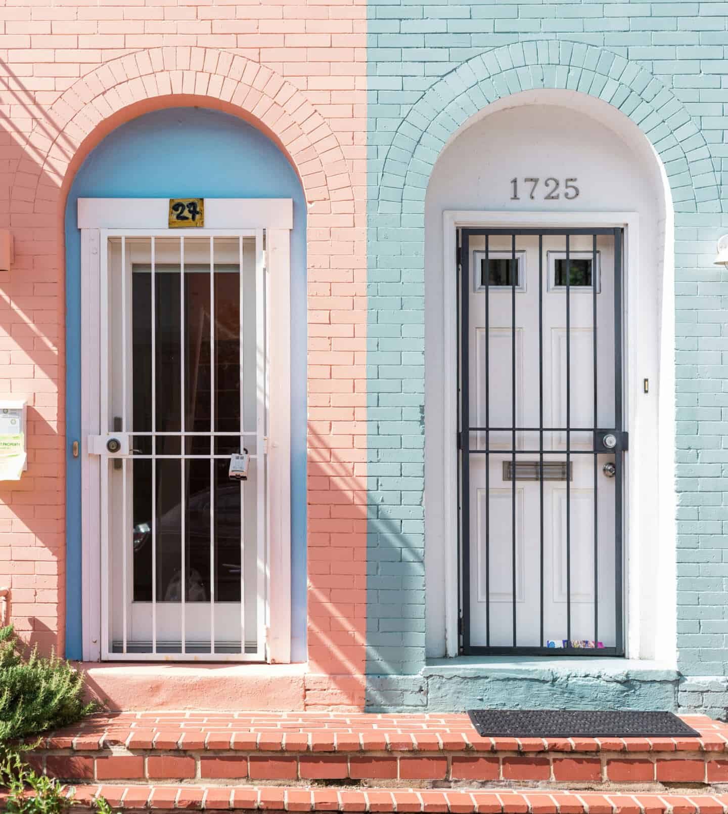 A pink building next to a blue building. both doors have bars on them for added home security