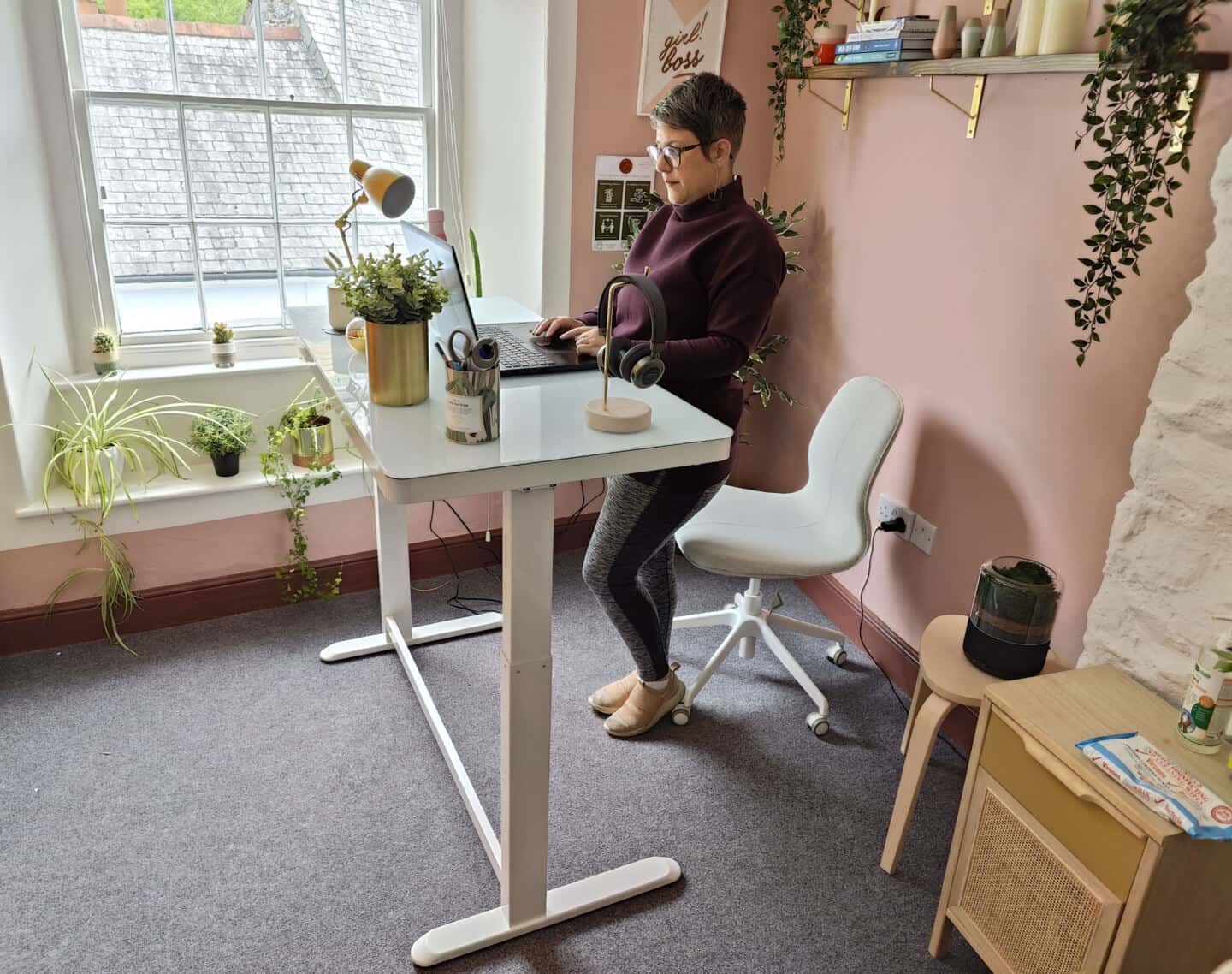 A white woman in her 40's works at the Flexispot EG8 Comhar Sit Stand Desk in standing position.