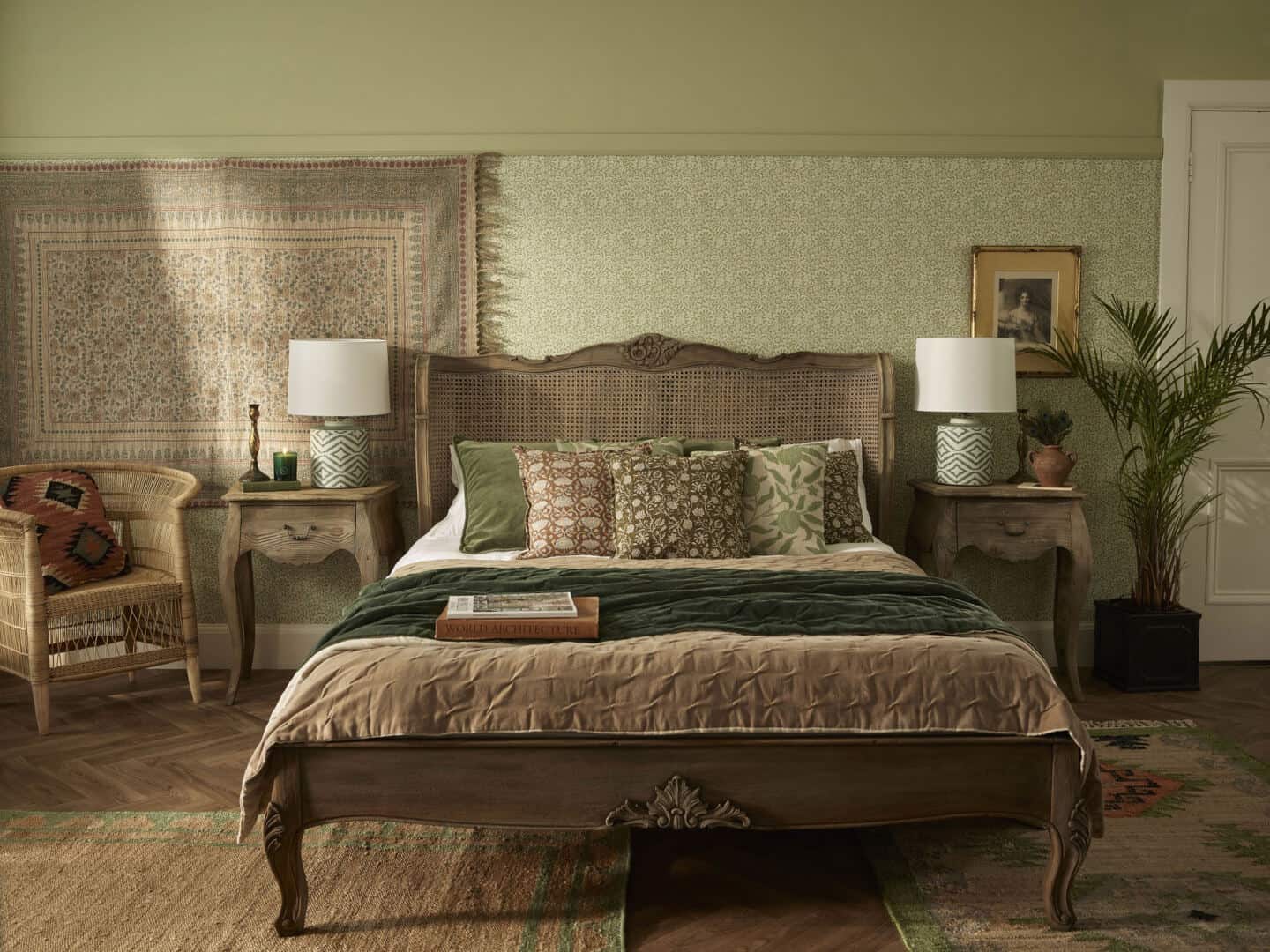 French style bed and two bedside tables. A wooden chair and plant on wither side of bed. Bedding made of natural materials. Two rugs on parquet flooring