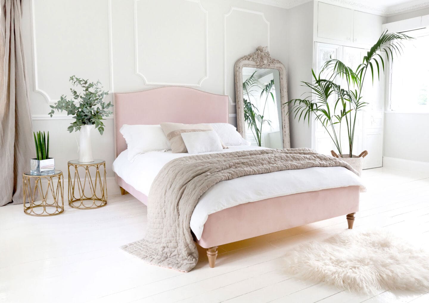 An elegant French bedroom style with white wood floorboards a sheep skin rug, double pink bed and lots of plants