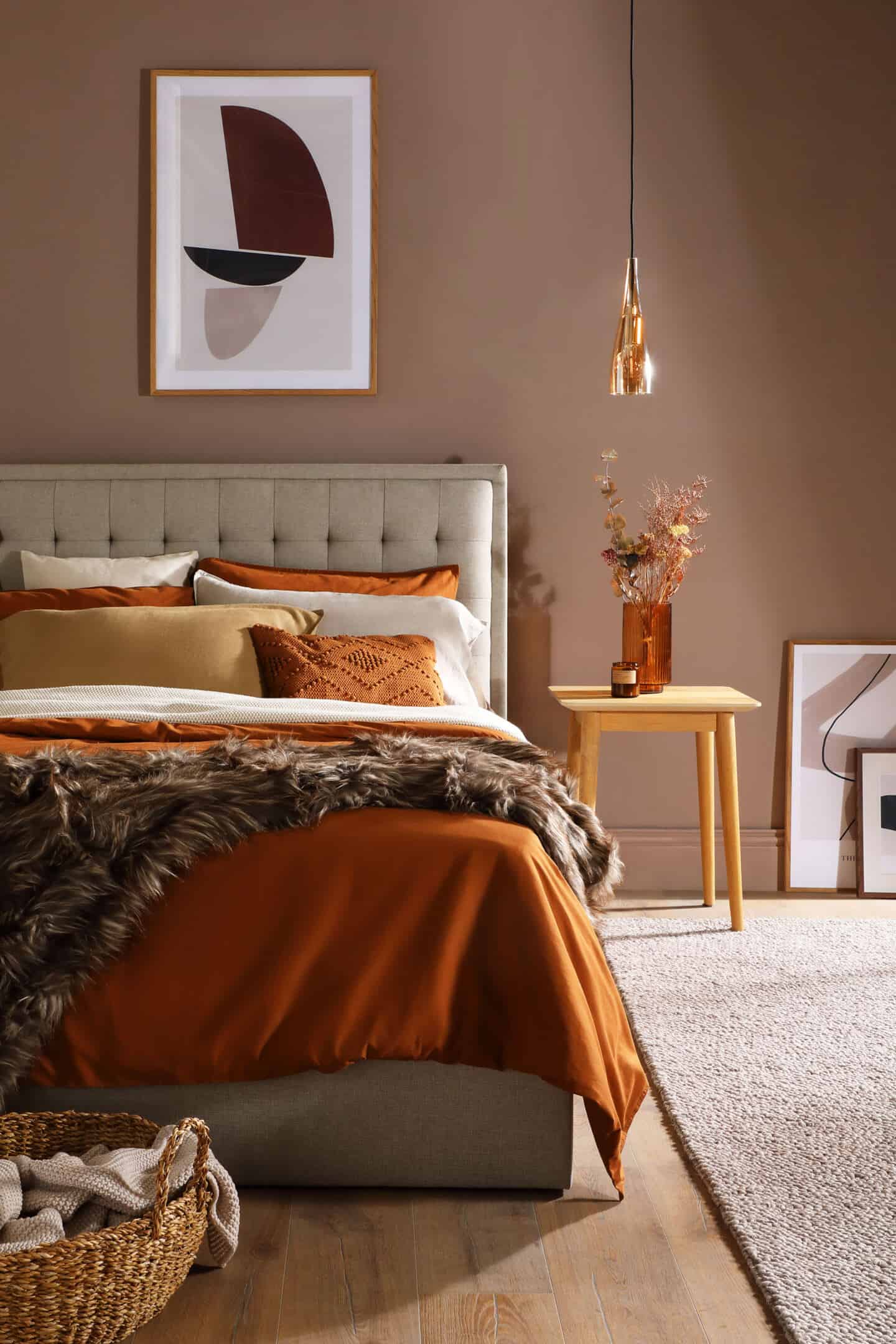 A bedroom featuring a fabric bed decked out in earthy coloured bedding with textured throw and pillow