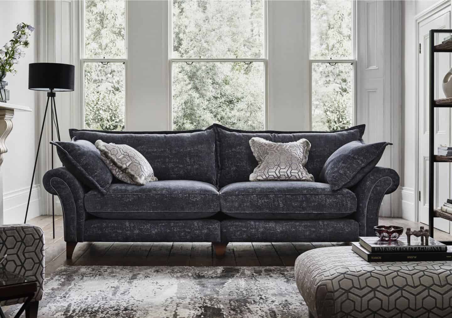 A grey English roll arm sofa with large white sash windows behind 