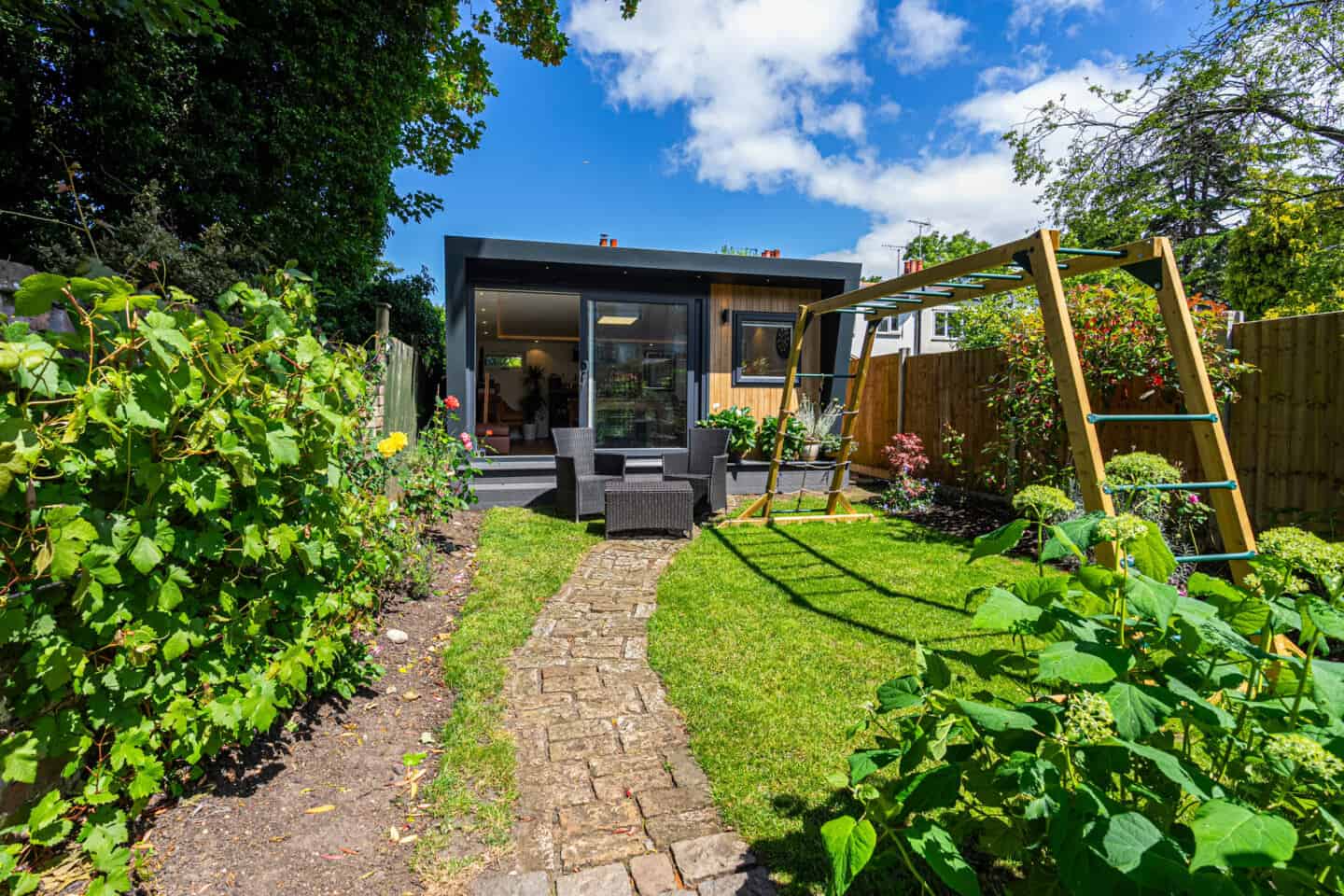 A low-maintenance garden featuring a garden room, two chars and a table and a children's climbing frame