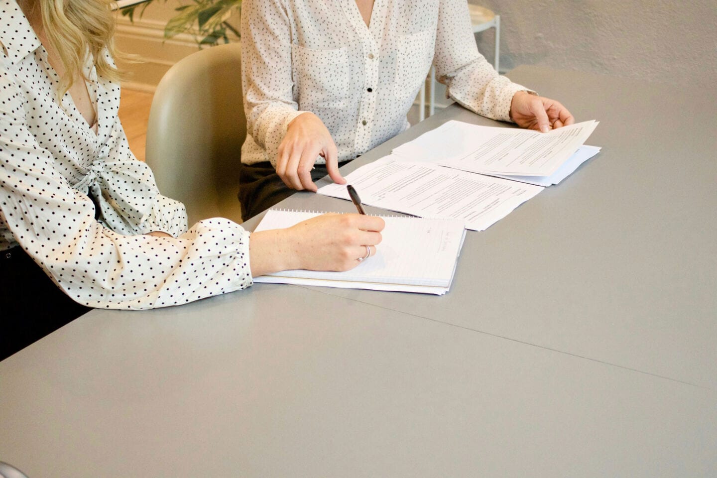 Two women sat at a desk looking at papers and taking notes