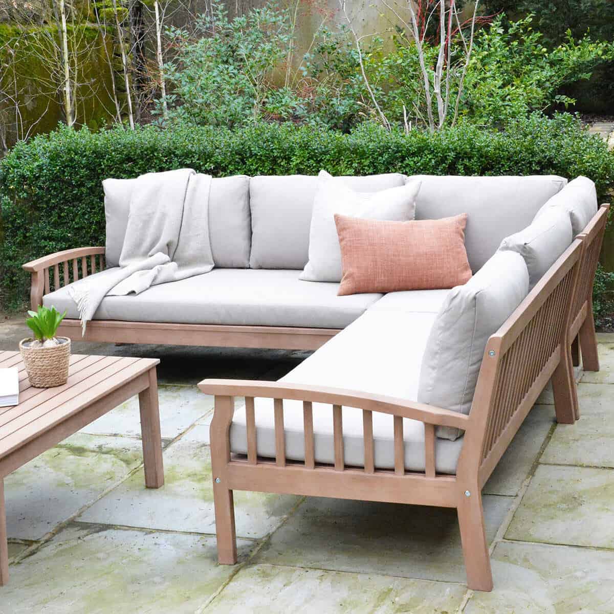 A teak corner garden sofa with grey cushions on a patio in the garden