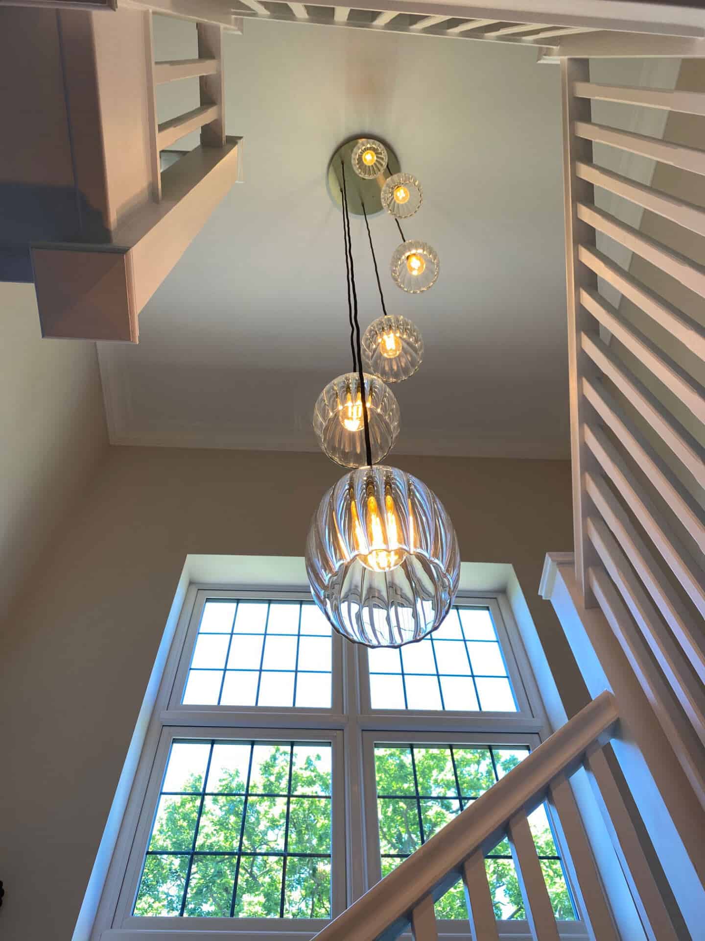 A view up at the ceiling in a stairwell. Fluted glass pedant lights in varying lengths hang down from the ceiling