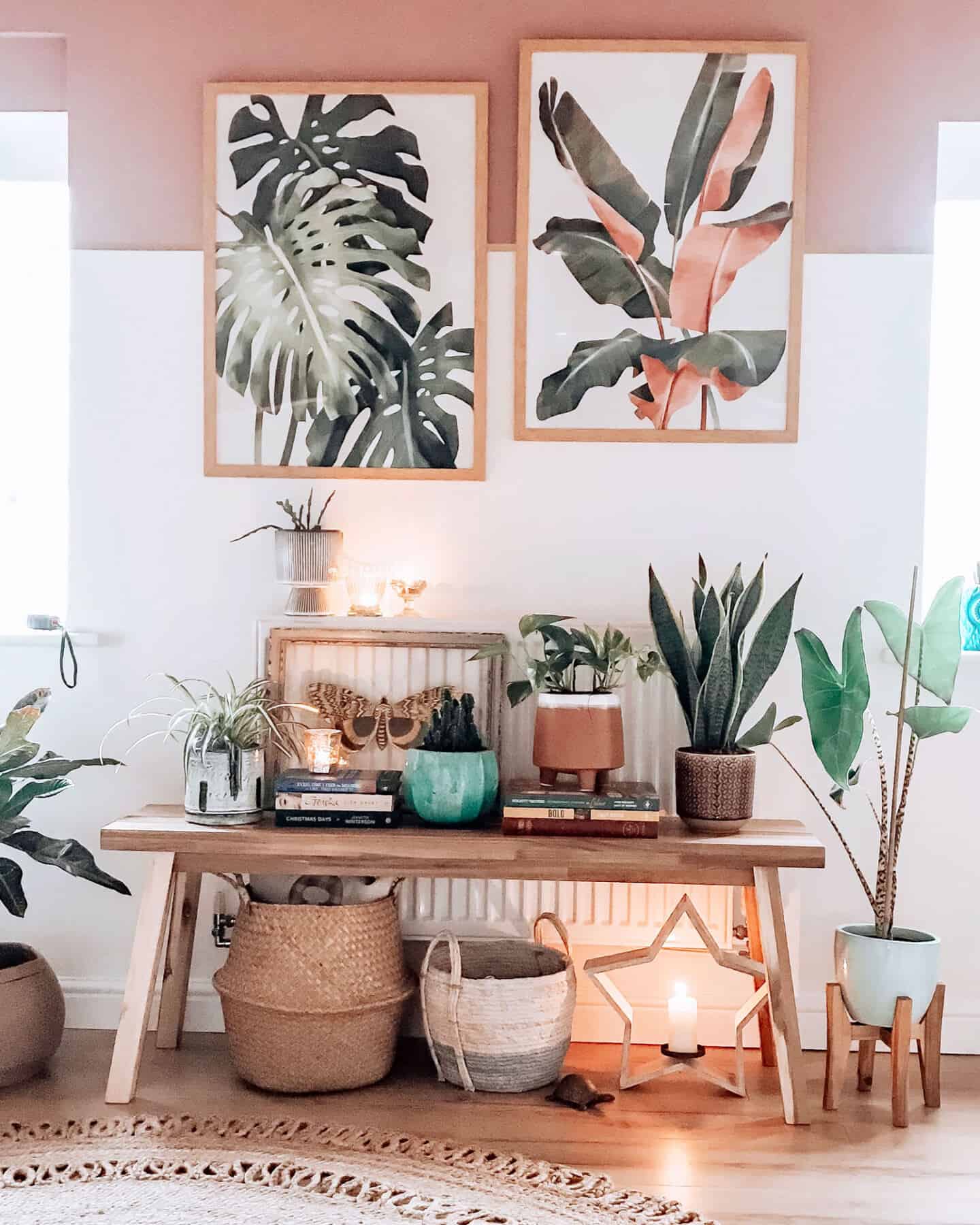 Botanical artwork inspired by Travel from Greenlili hung on a white and pink wall above a wooden bench covered in plant pots