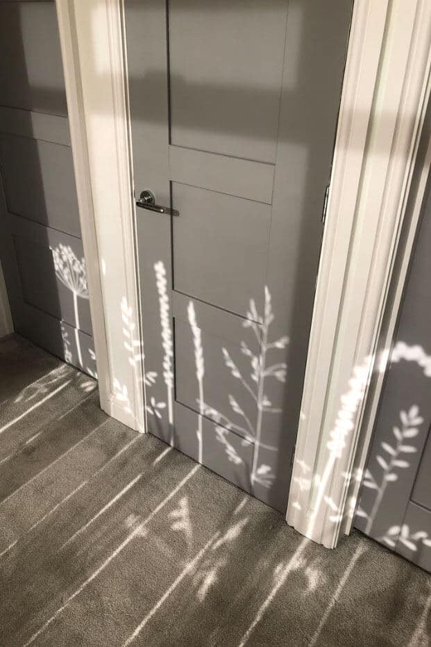 shadows cast across the floor and wall of meadow flowers created by the sunlight coming through the  window film