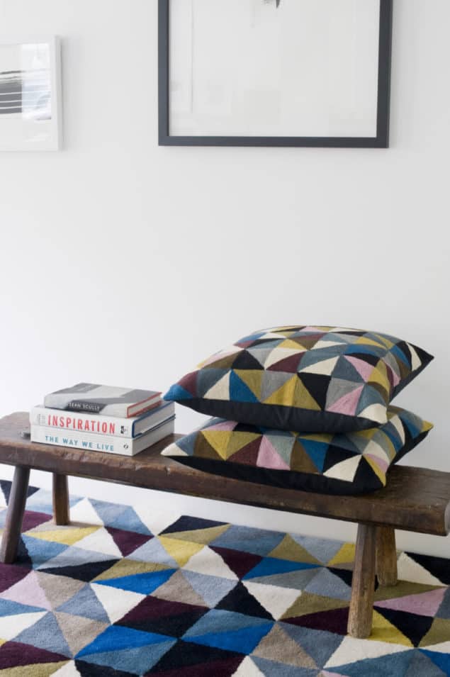 Geometric cushions placed upon a bench which rests on a geometric rug by Niki Jones