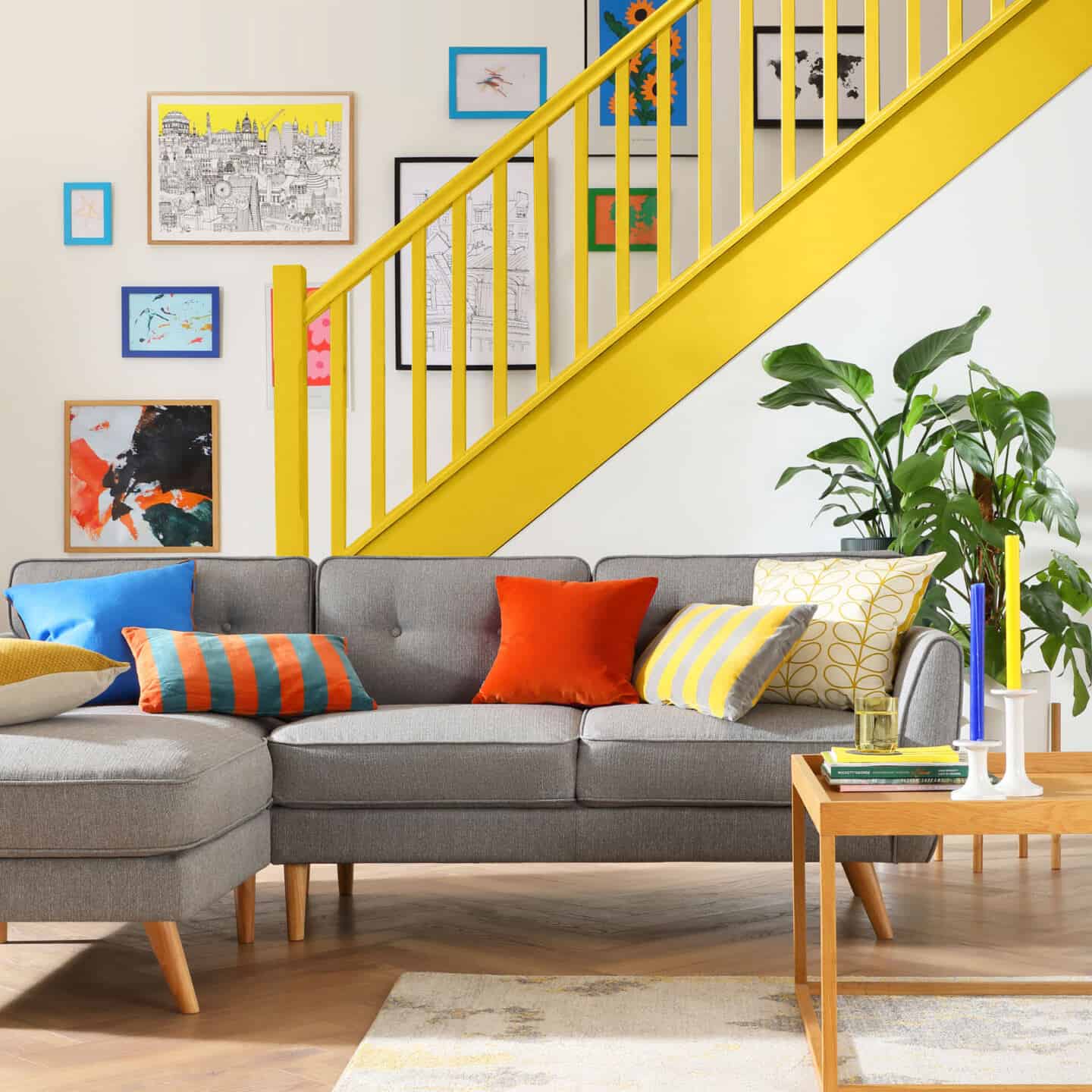 A living room with a bright yellow staircase behind a grey sofa