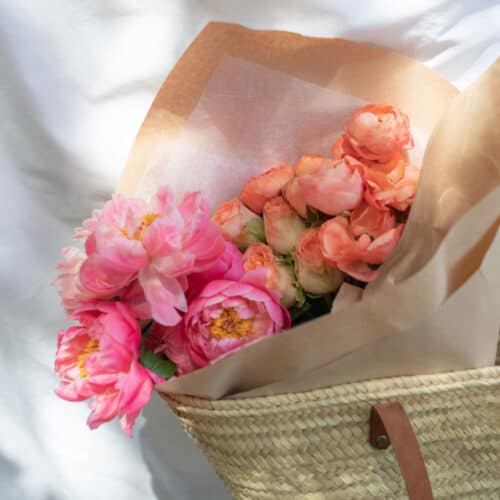 Pink Peony flowers wrapped in paper inside a woven palm leaf bag