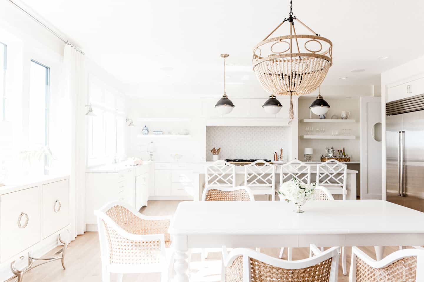 A bright white modern kitchen featuring dining table with wooden white chairs and a rattan ceiling light above.