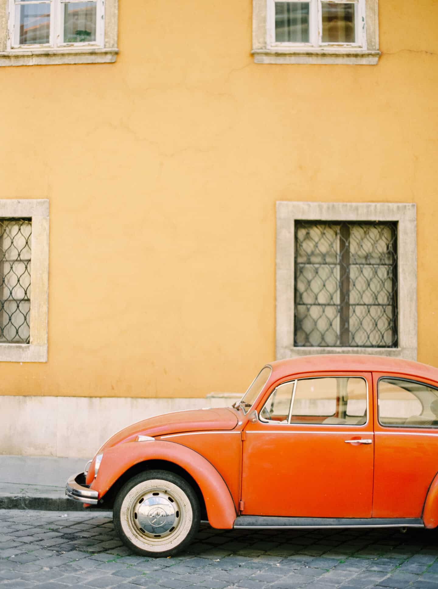 An orange VW Beetle parked in a European street against a yellow building