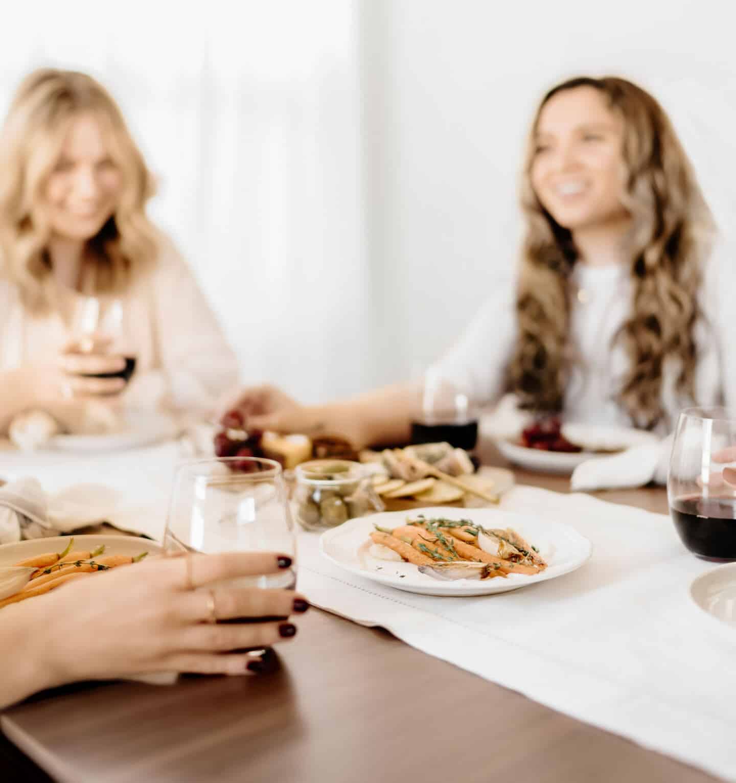 Three young expat women sat around sharing a meal and some red wine