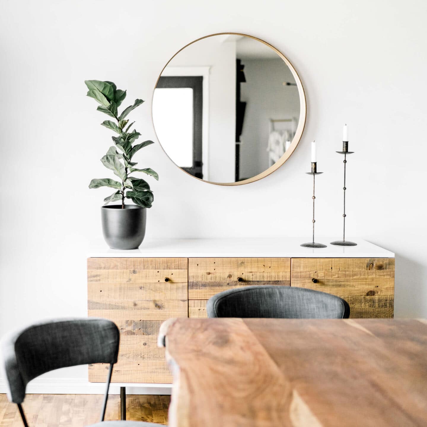 A dining room with living edge wooden table, wooden side board and a round mirror on the wall