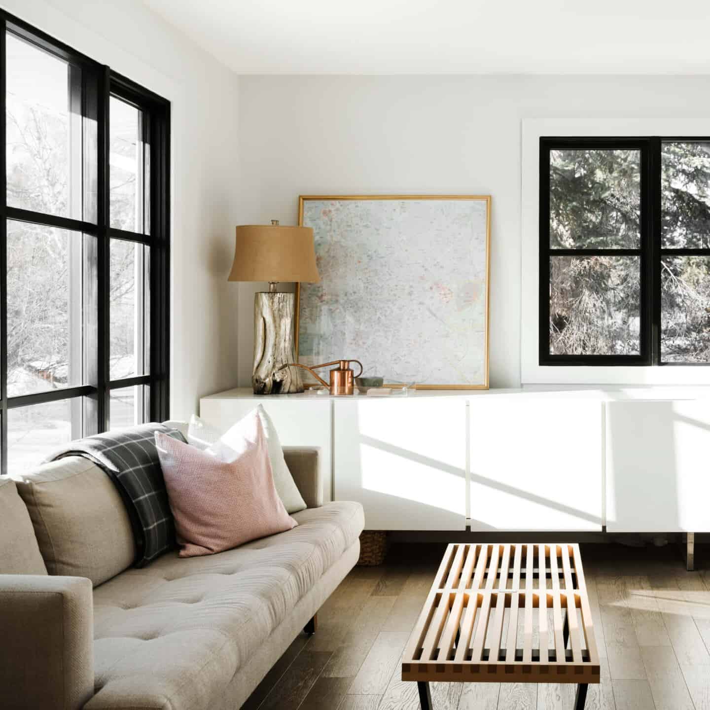 A modern living room with double aspect black framed windows, a white sideboard and grey sofa