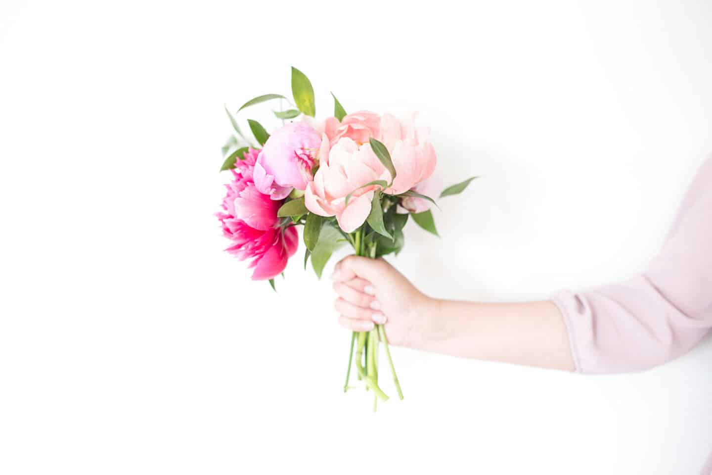 A white woman's arm holding a bunch of pink peony flowers