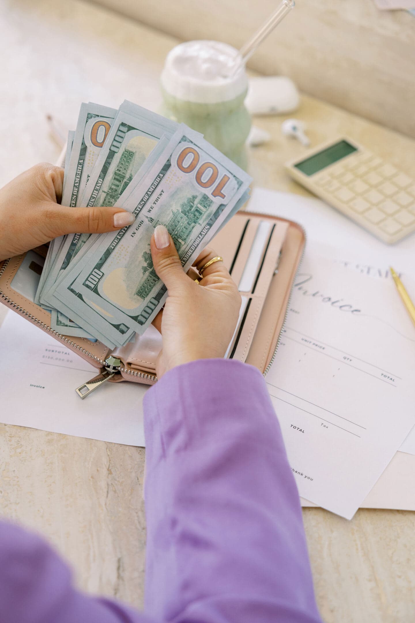 A woman holding hundred dollar bills she has taken from her purse to pay invoices.