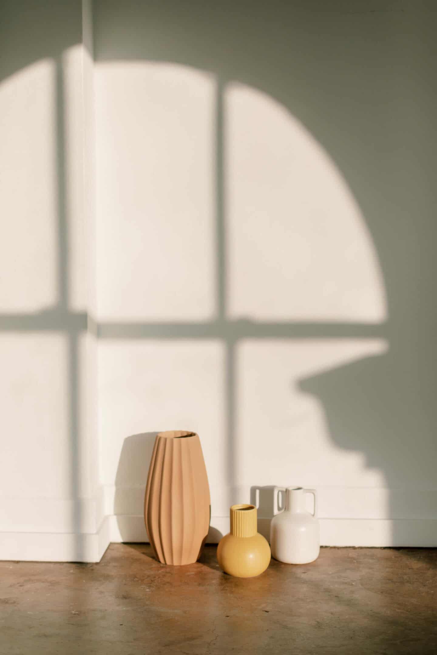 3 vases on a wooden floor with a white wall behind 