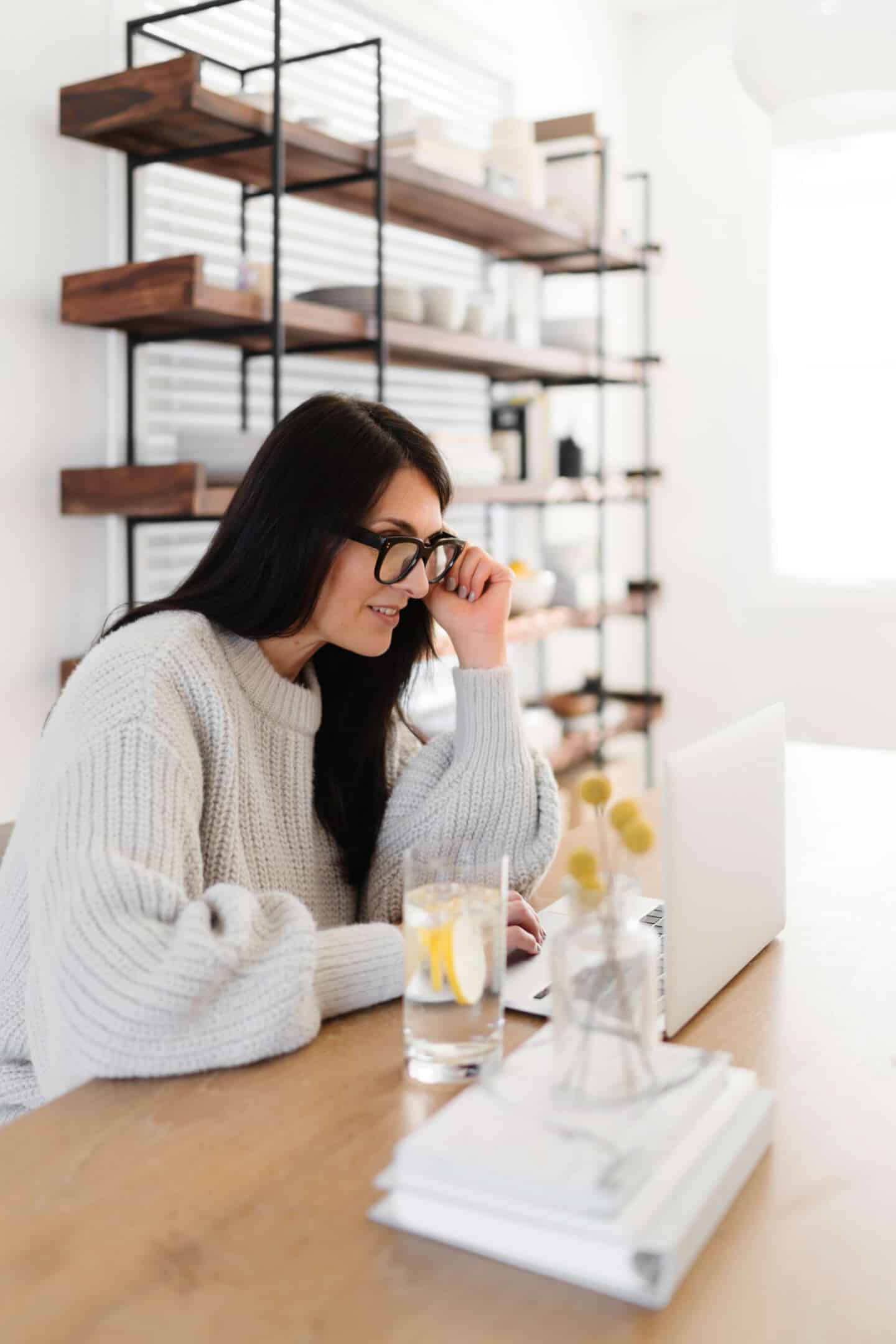 A middle aged woman in glasses sat at a desk working on a laptop