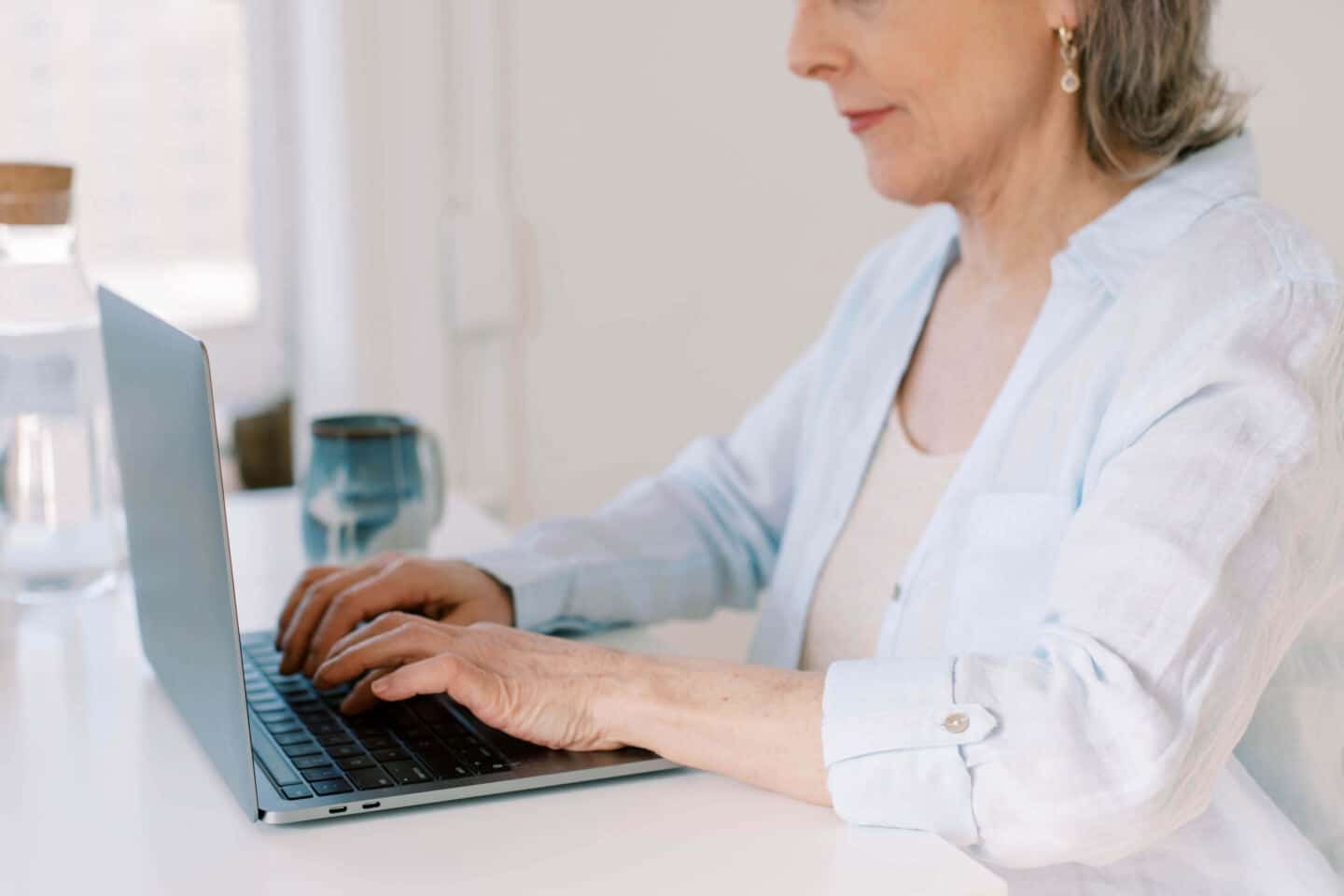 An older woman sits typing on a laptop