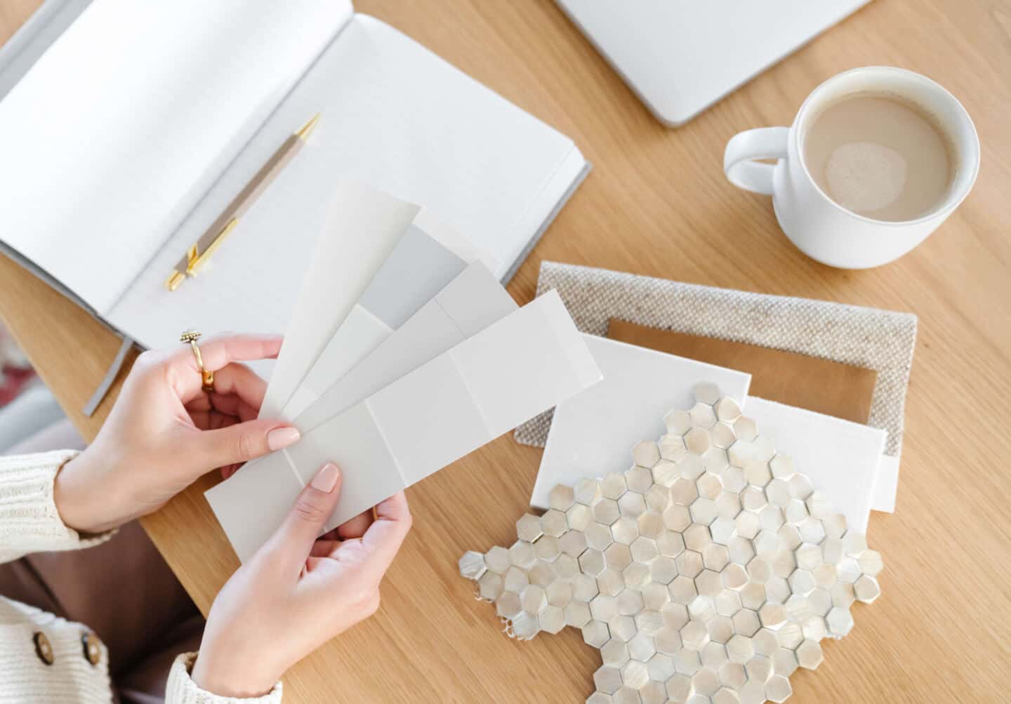 A woman's hands hold paint chits above a notebook and next to fabric and tile samples for an interior design project