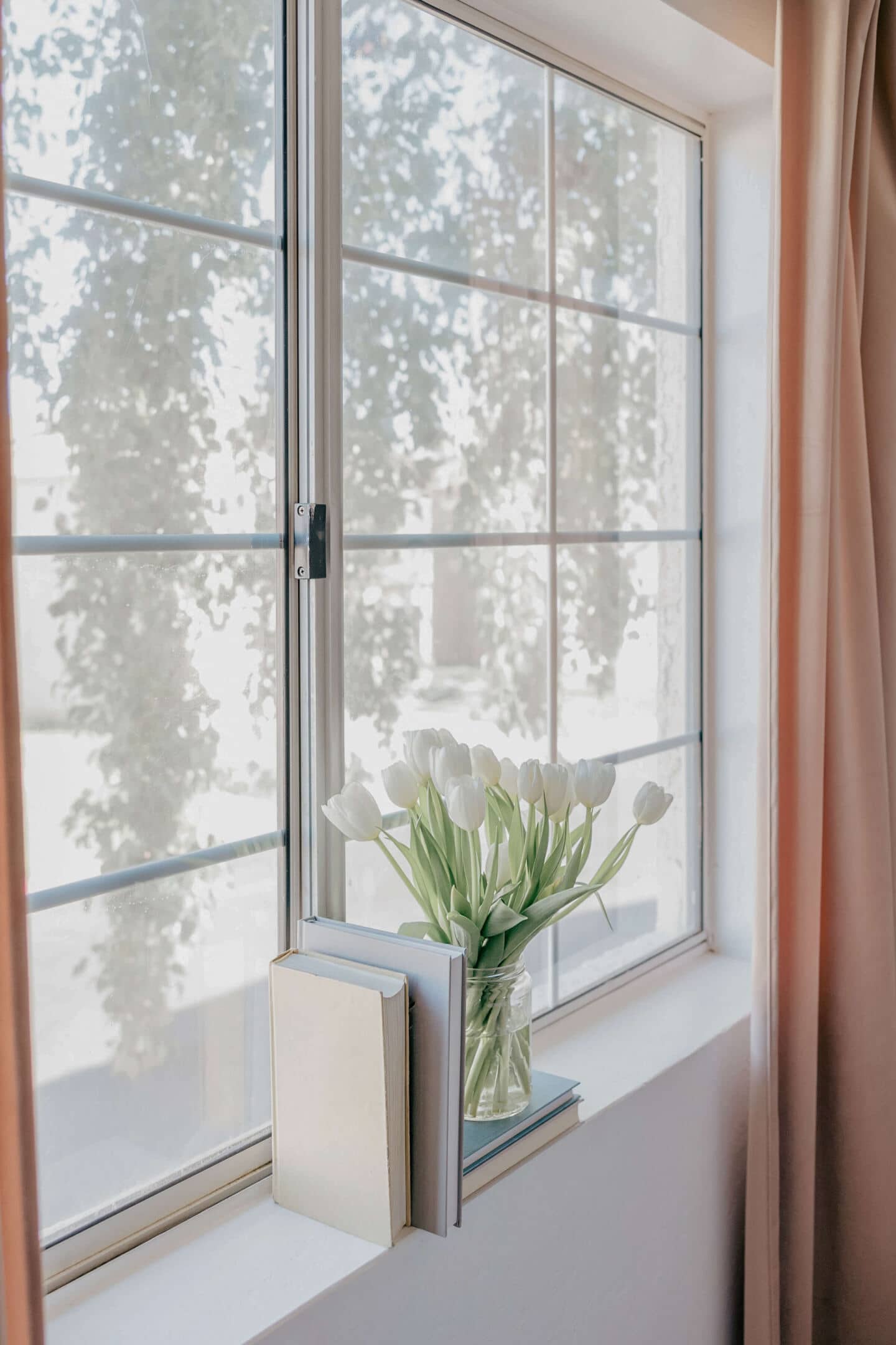 A bunch of white tulips on a window sill next to some books