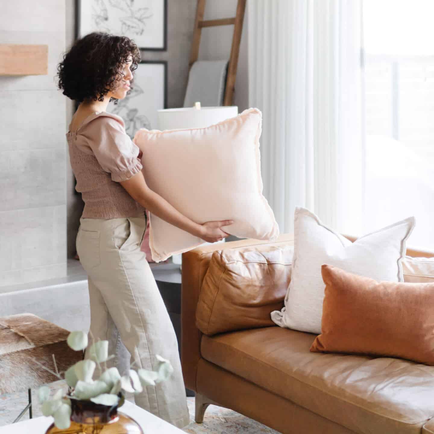 A young woman adding cushions to a brown leather sofa