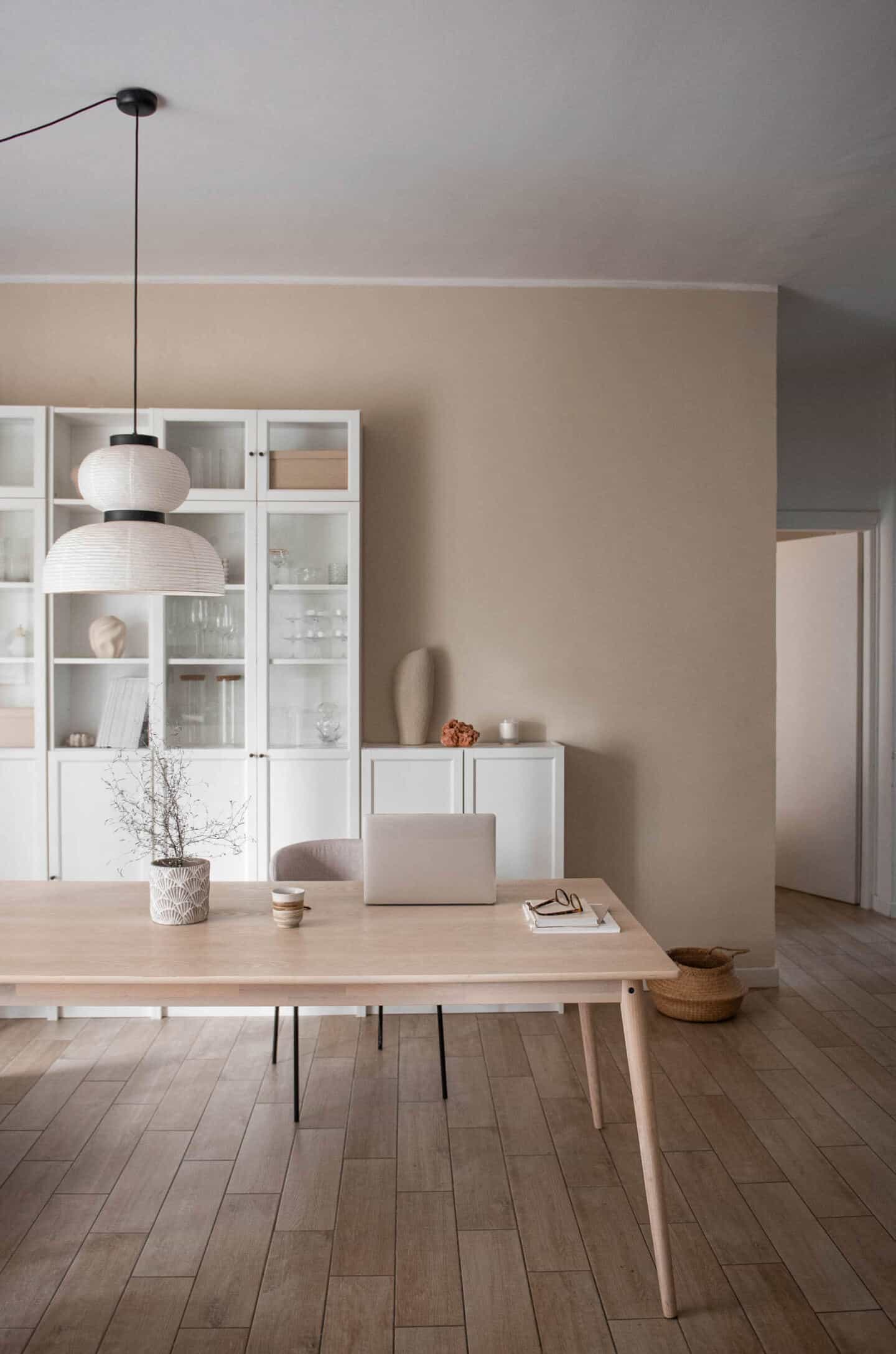 A dining room featuring a large white oak table with a laptop on it and storage shelves behind