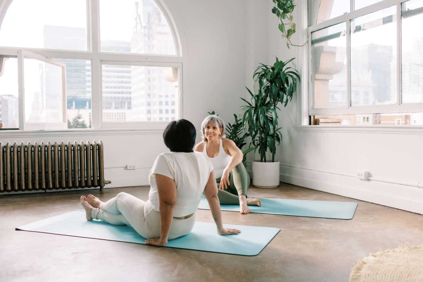 Two older women sat on yoga mats in a fitness studio