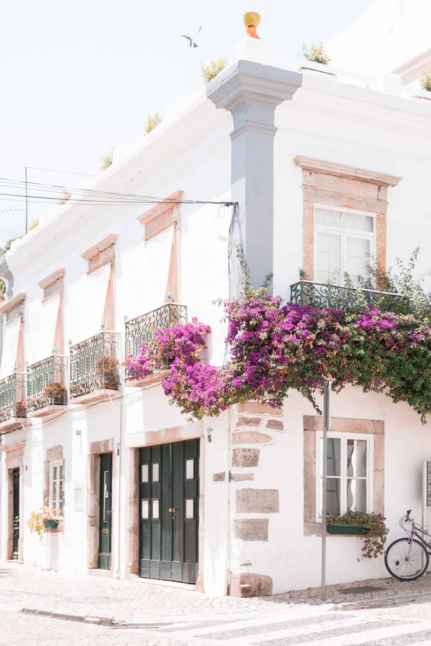 The exterior of a Mediterranean townhouse with small balconies covered in pink flowering plants