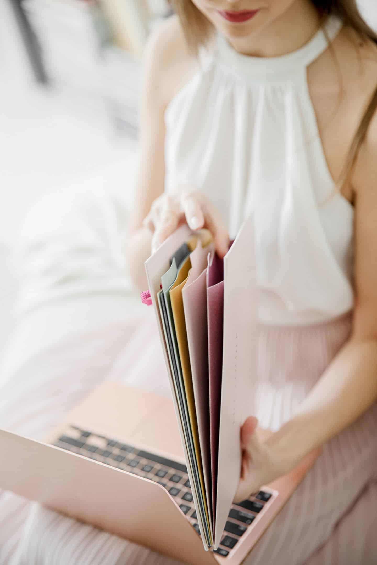 A young woman sat with a laptop on her lap looking through some paper files.