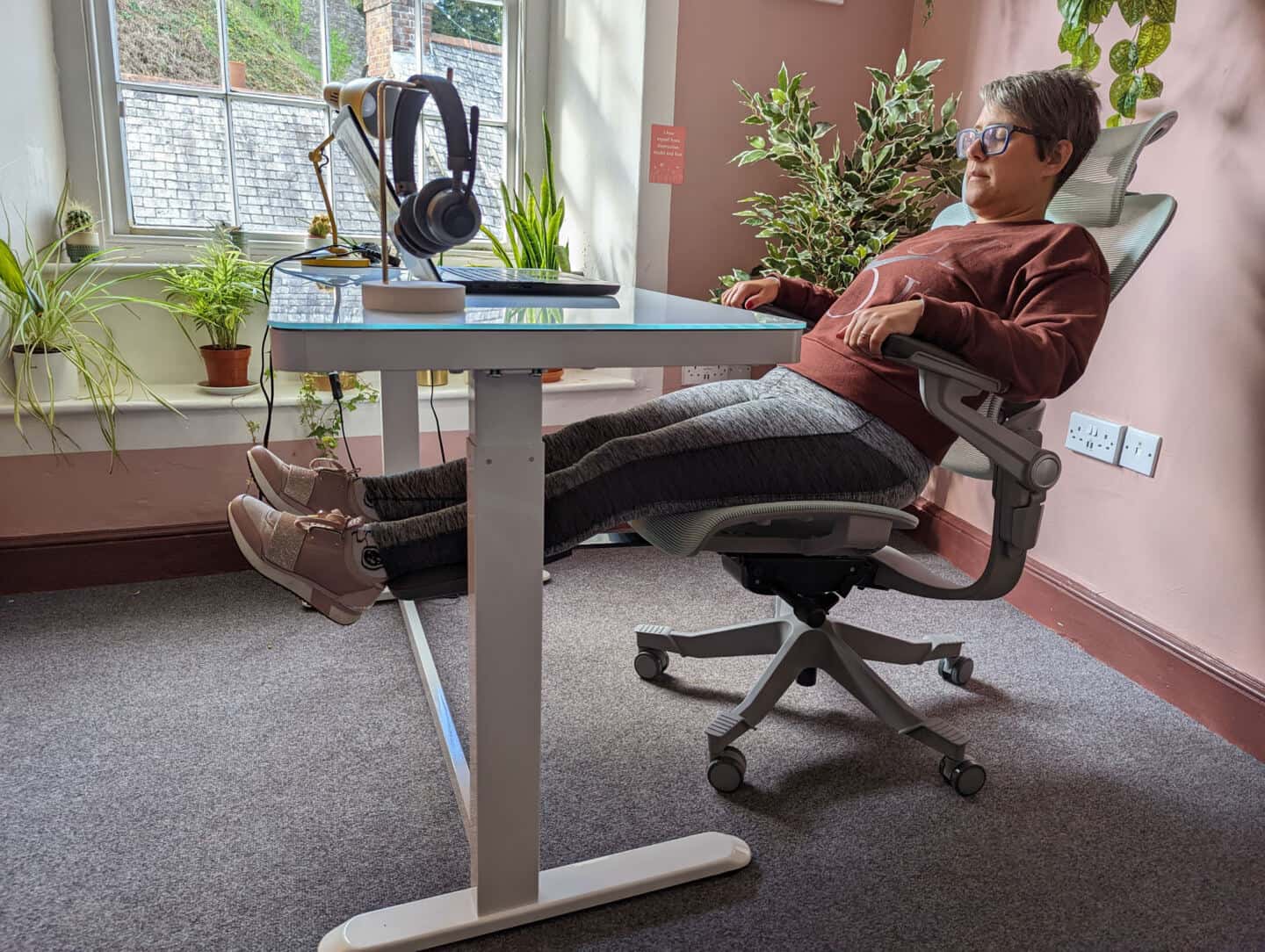 A woman reclined in a Hinomi H1 Pro office chair in a pink office surrounded by plants