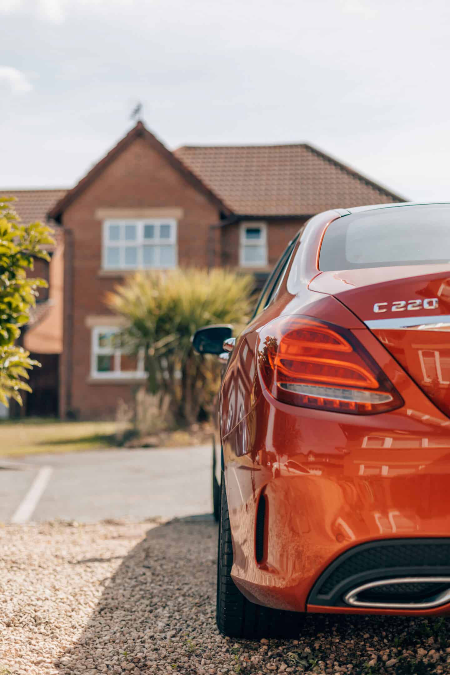 A red Merecedes parked on a gravel driveway with a red brick house in the background