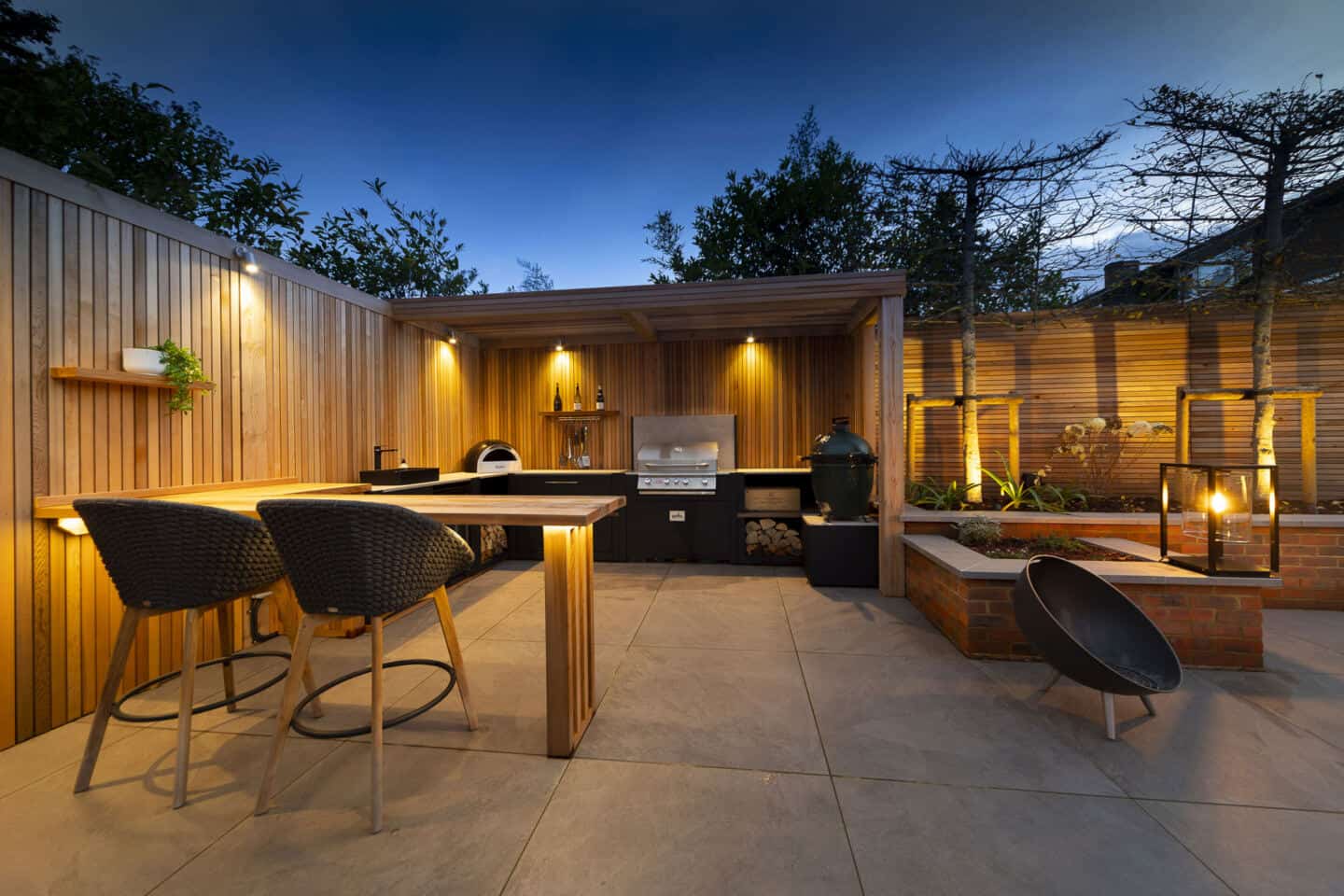 A patio garden with outdoor kitchen is illuminated at night