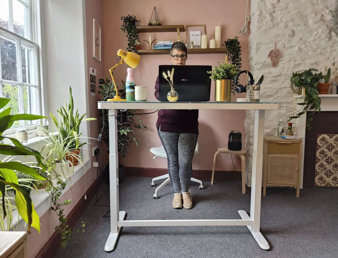 A white woman in her 40's works at the Flexispot EG8 Comhar Sit Stand Desk in standing position.