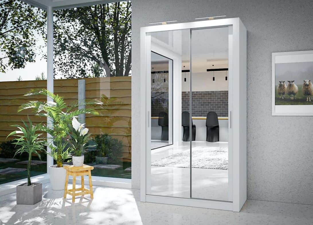 A white wardrobe with mirrored sliding wardrobe doors in a minimalist room with large glass extension. A kitchen can be seen in the reflection.