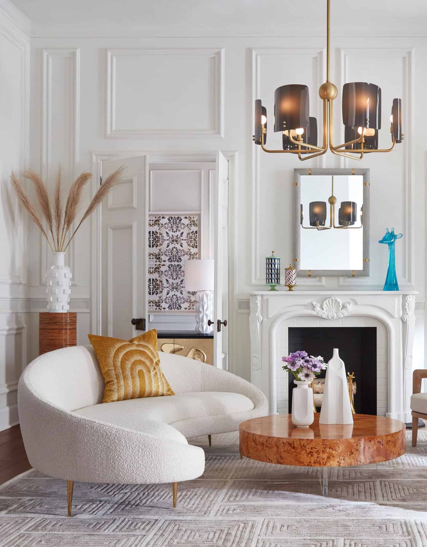 A curved white bouclé sofa with a round wooden coffee table in front of a fireplace