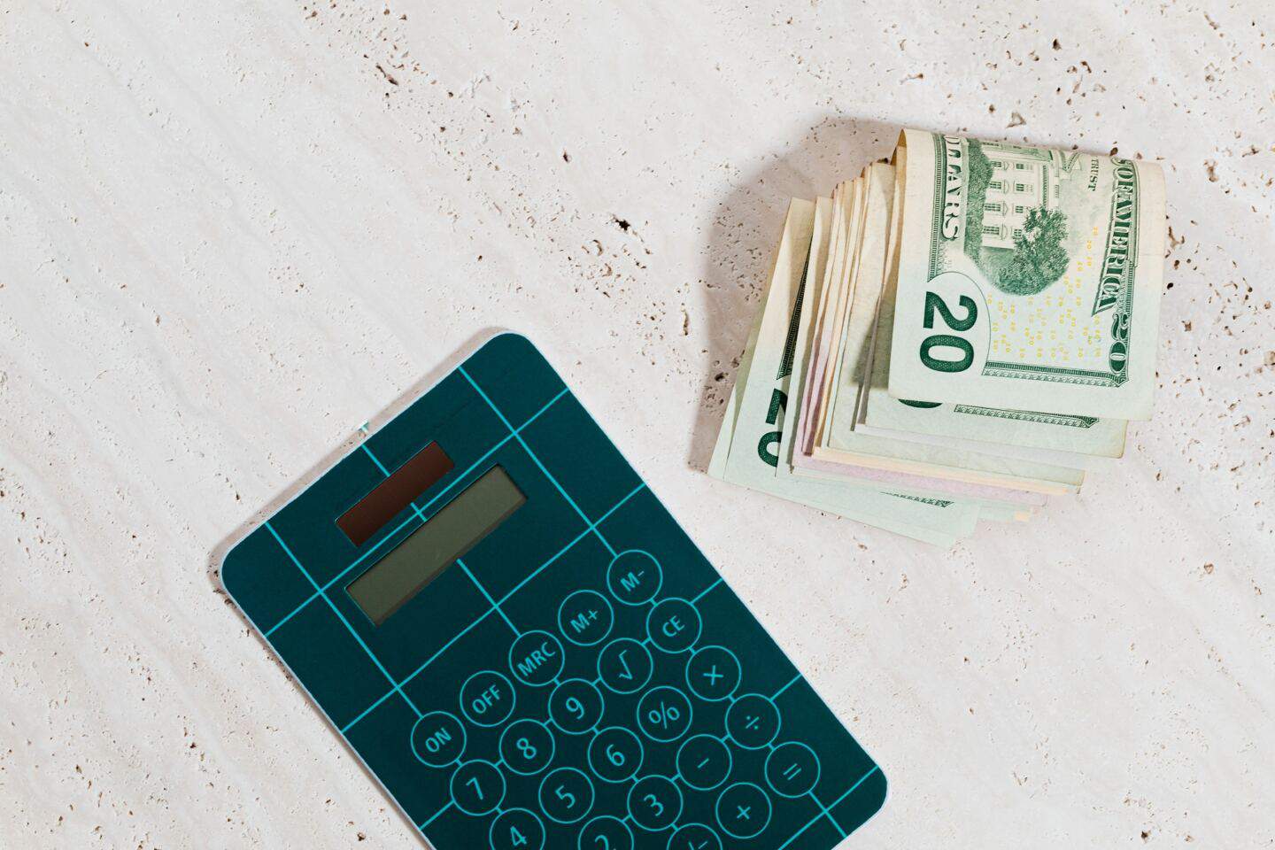 A calculator and a wad of bank notes on a concrete surface