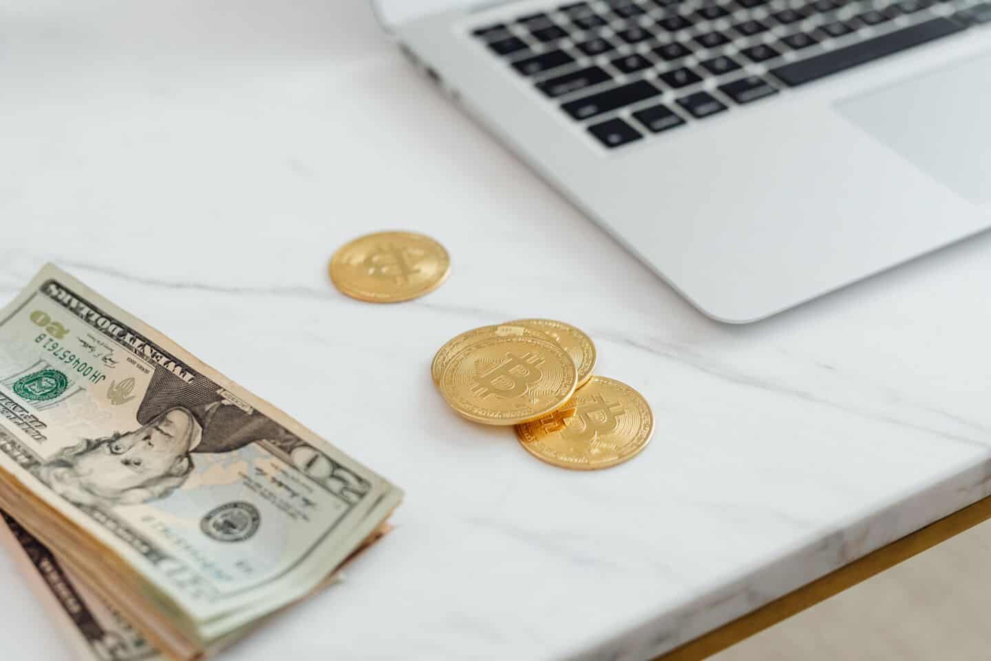 A laptop next to paper money and coins on a work surface