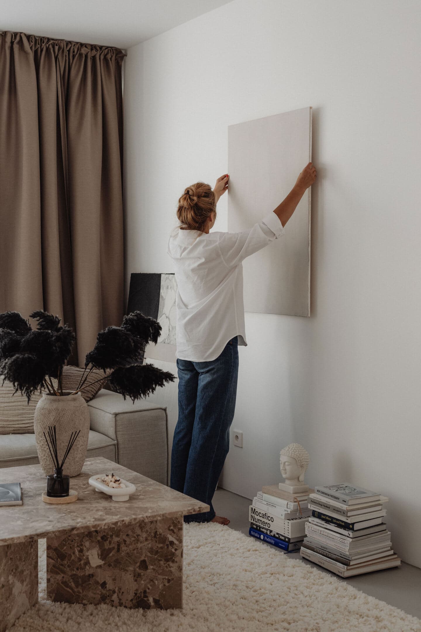 A woman hangs a picture on the wall of a living room