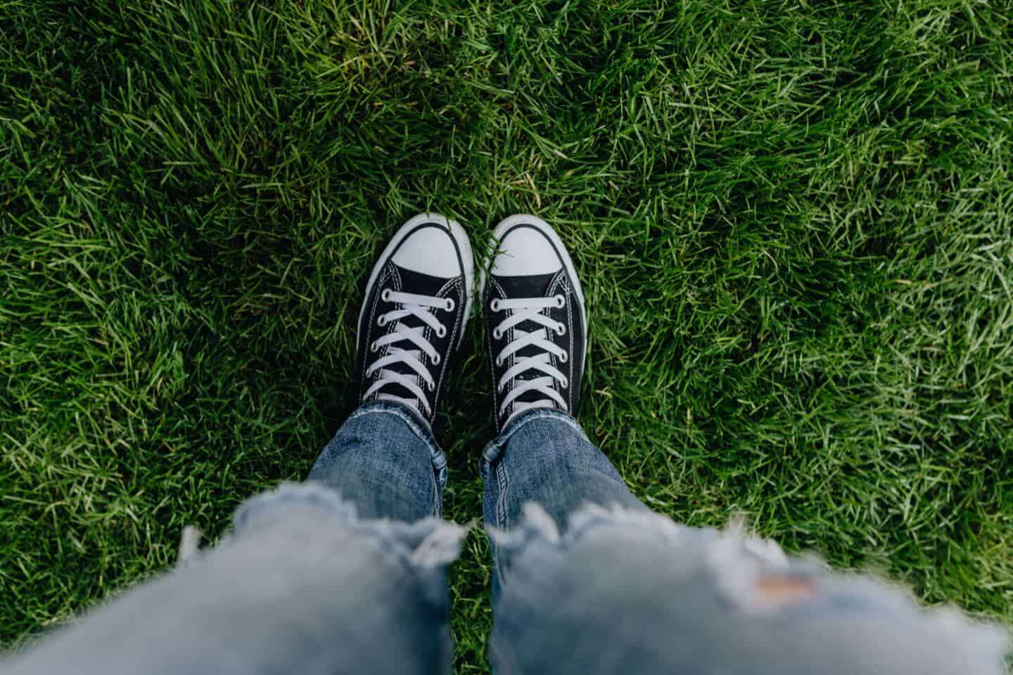 A woman wearing Converse shoes stood on a lush green garden lawn