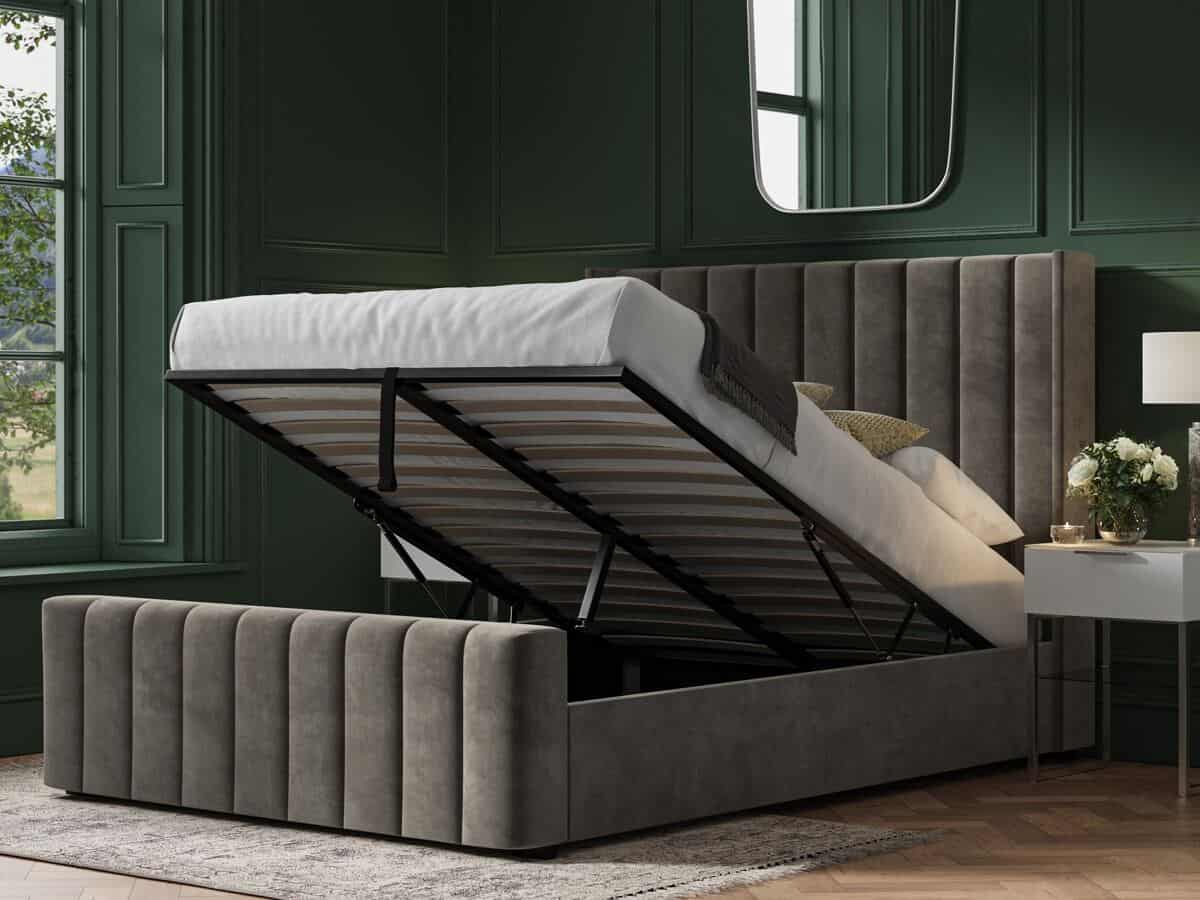 A moss green bedroom featuring a large grey ottoman bed with storage. The mattress is elevated but you cannot see what is inside