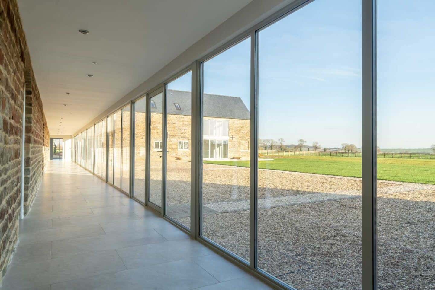 A lengthy corridor with aluminium sliding doors down one side of barn conversion  