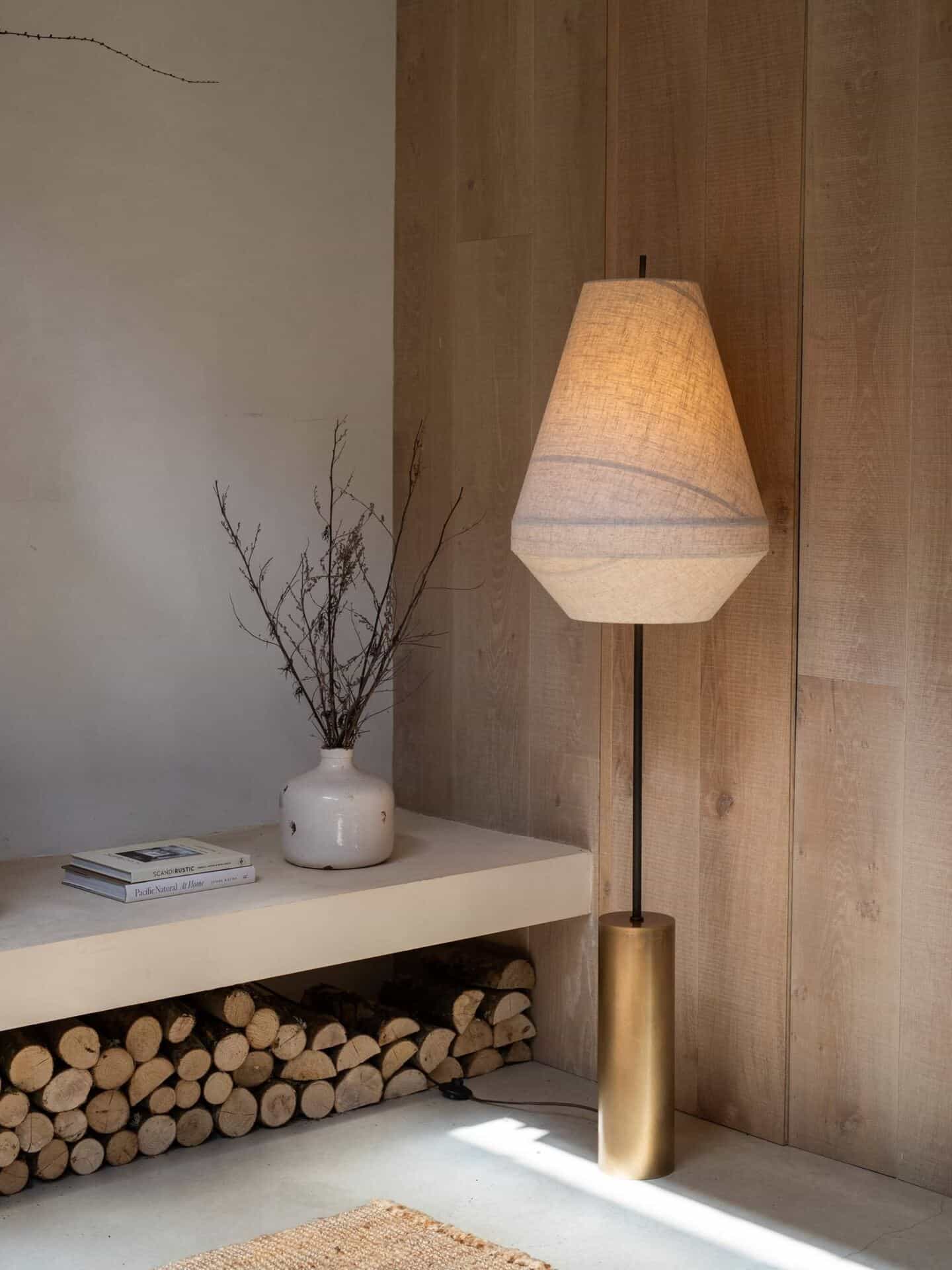 A hallway with bench seating and logs stored beneath. A linen floor lamp glows in the corner